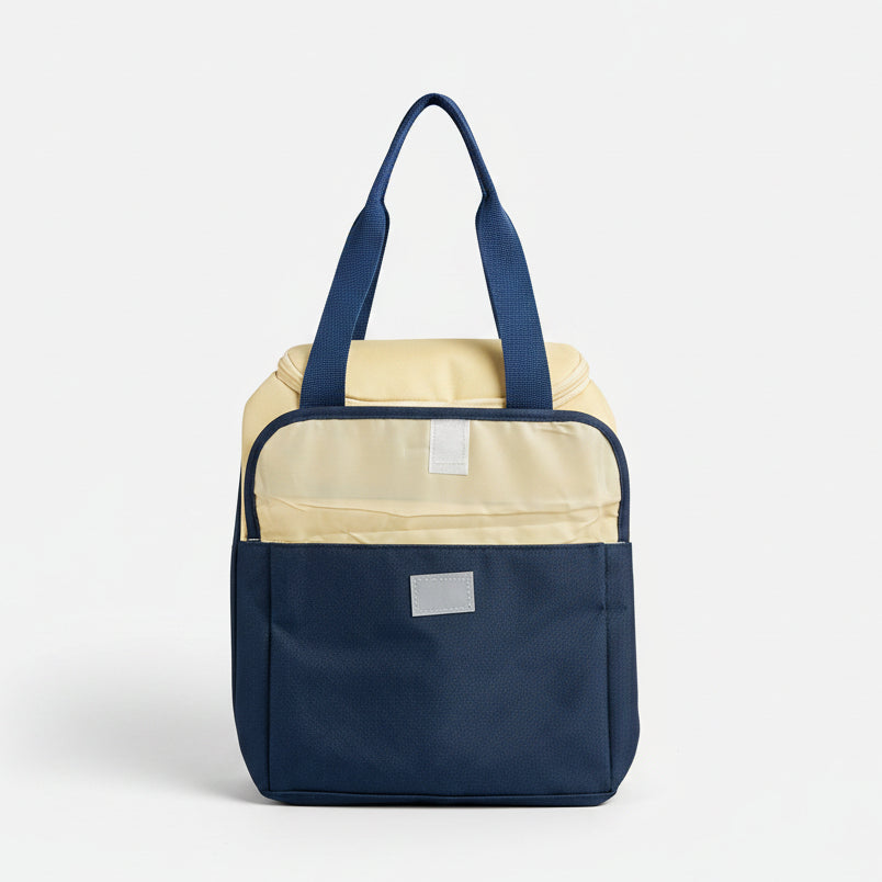 A two-tone soft-sided bag with a navy blue lower half and a cream upper half, featuring blue handles and a small white rectangular patch on the front, set against a neutral gray background.