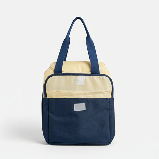 A two-tone soft-sided bag with a navy blue lower half and a cream upper half, featuring blue handles and a small white rectangular patch on the front, set against a neutral gray background.